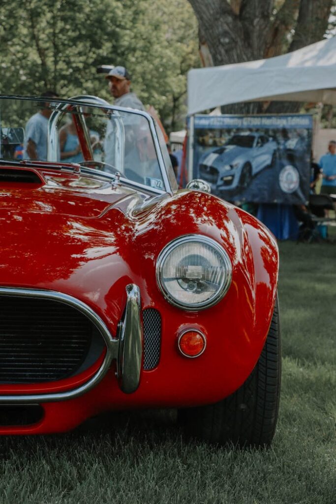 Vintage red Shelby Cobra close-up with headlight detail at outdoor car show.