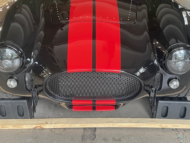 Front view of a black Cobra replica with red racing stripes and a perforated grille in the nose opening