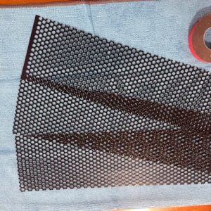 Close view of black powder-coated perforated aluminum screen blanks and mounting tape
